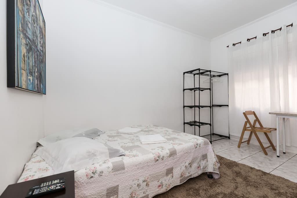 Vista da sala com a cama de casal, arara com estantes