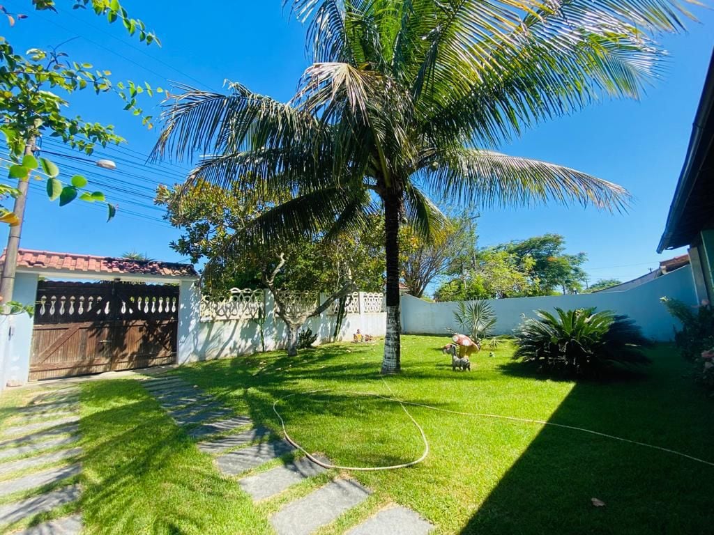 A landscaped garden features a palm tree and various greenery, with stone pathways leading through the lawn. The bright blue sky provides a sunny backdrop, and a wood gate is visible in the distance, adding to the outdoor ambiance.