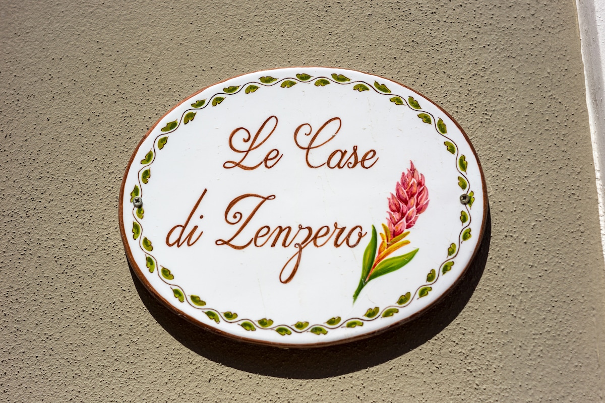 A decorative sign reading 'Le Case di Zenzero' is displayed on a textured wall. The sign features a flower illustration, enhancing its visual appeal and providing a welcoming touch for guests.