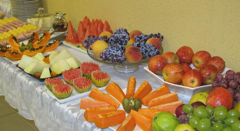 A generous breakfast spread is displayed on a white tablecloth, featuring a variety of fresh fruits, including papaya, watermelon, blueberries, apples, and grapes. Colorful slices of melons and a selection of cheeses are also arranged neatly, providing a vibrant and inviting start to the day.