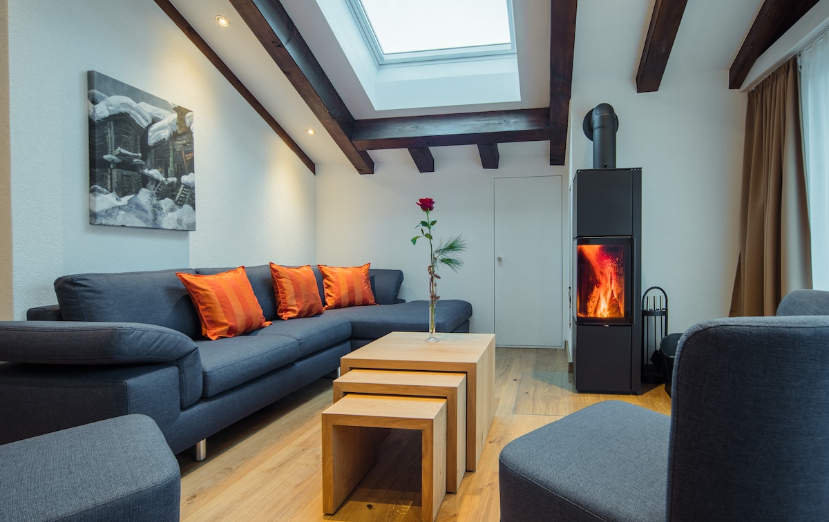A spacious living area features a sectional sofa adorned with orange pillows, a wooden coffee table, and a contemporary fireplace. Two clerestory windows allow natural light to fill the room, enhancing the warm ambiance.