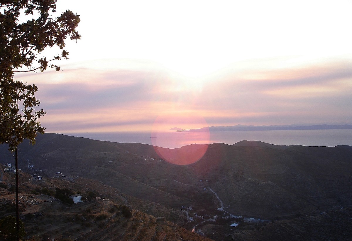 A stunning view of the Aegean Sea is presented at sunset, with soft hues of pink and purple blending across the sky. Rolling hills and distant islands are visible, creating a serene landscape that invites relaxation and appreciation of nature's beauty.