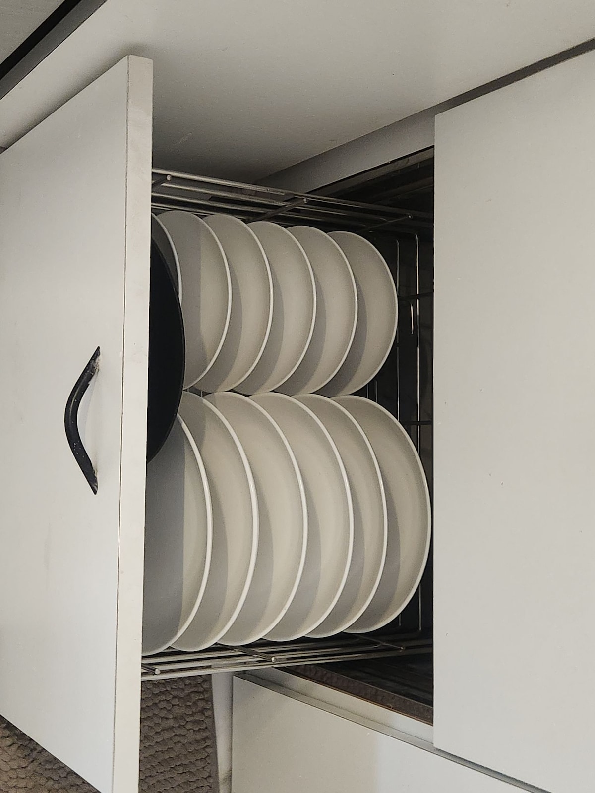 A metal dish rack is shown with multiple white plates organized neatly. The rack is located in a drawer, revealing a smooth interior and a clean, minimalist design. The plates are arranged in a way that allows for easy access.