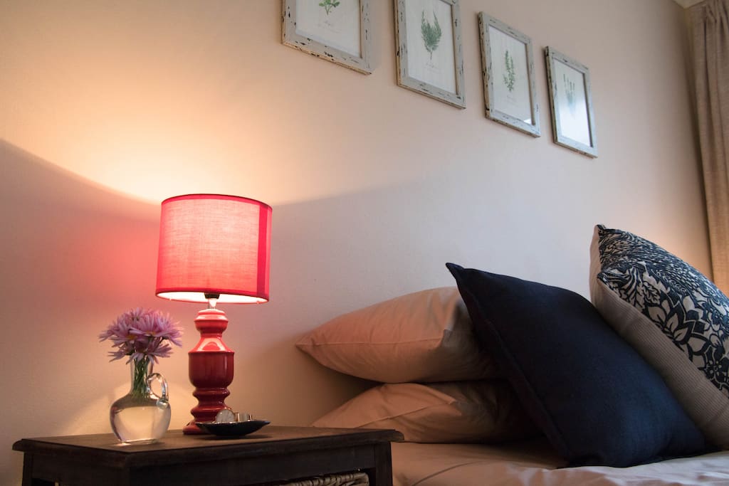 The main bedroom features a queen-size bed with ample bedding, an armchair, a fan, a heater, and a small desk area.