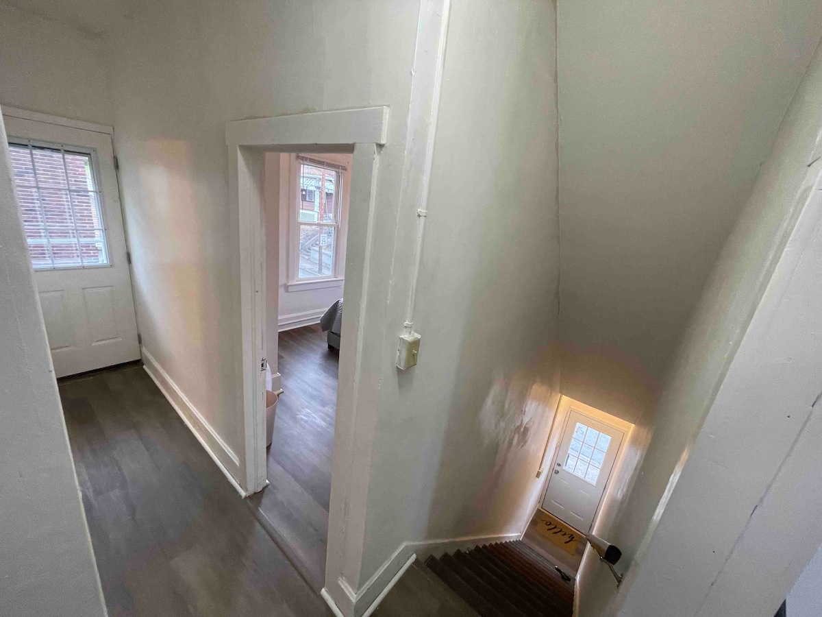 De gang naar de zijdeur kijkt de trap af naar de voordeur, met de slaapkamer in de middelste badkamer links, de woonkamer rechts en de keuken erachter. 