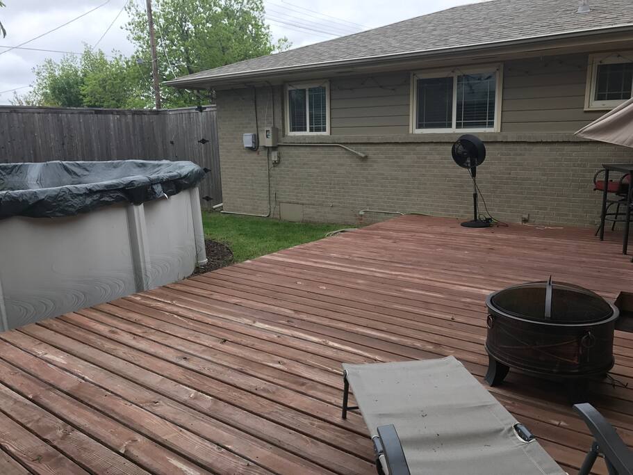 Back deck with tall privacy fence, pool, fire pit, deck furniture and misting fan.