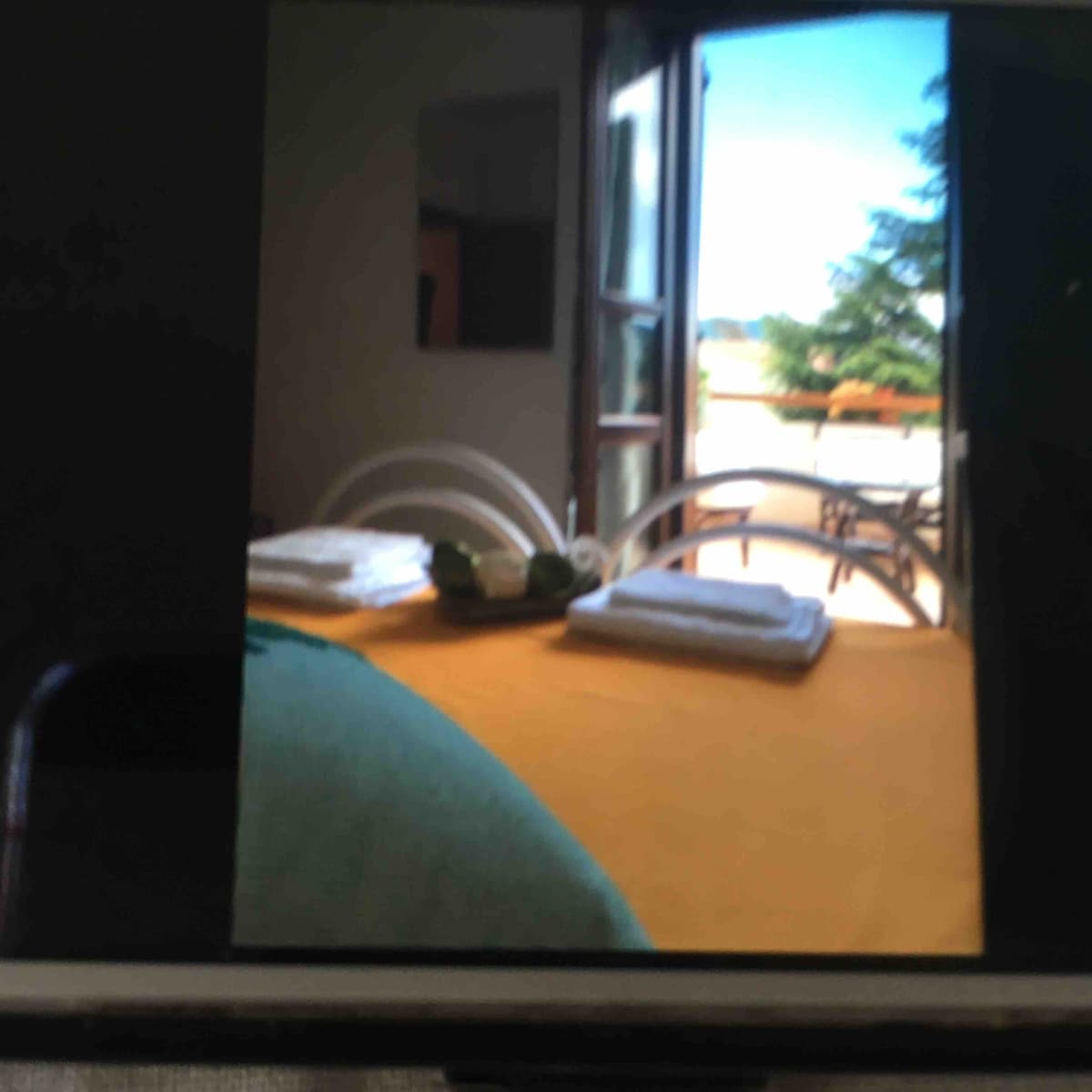 Natural light enters through open double doors, revealing a view of greenery outside. A table is set with neatly stacked towels, accompanied by decorative items. The scene suggests a welcoming outdoor space, enhancing relaxation in the setting.