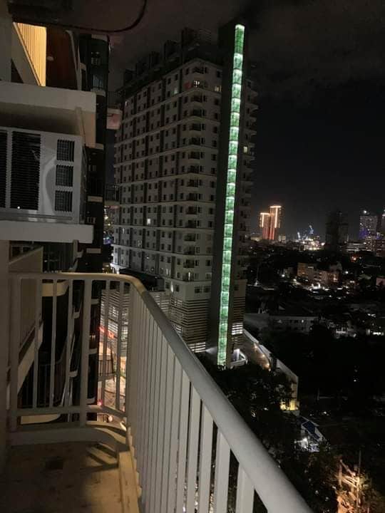 A spacious balcony offers an unobstructed view of the urban skyline at night, featuring illuminated buildings. The railing provides safety while taking in the city lights and the contrasting glow of neighboring structures.