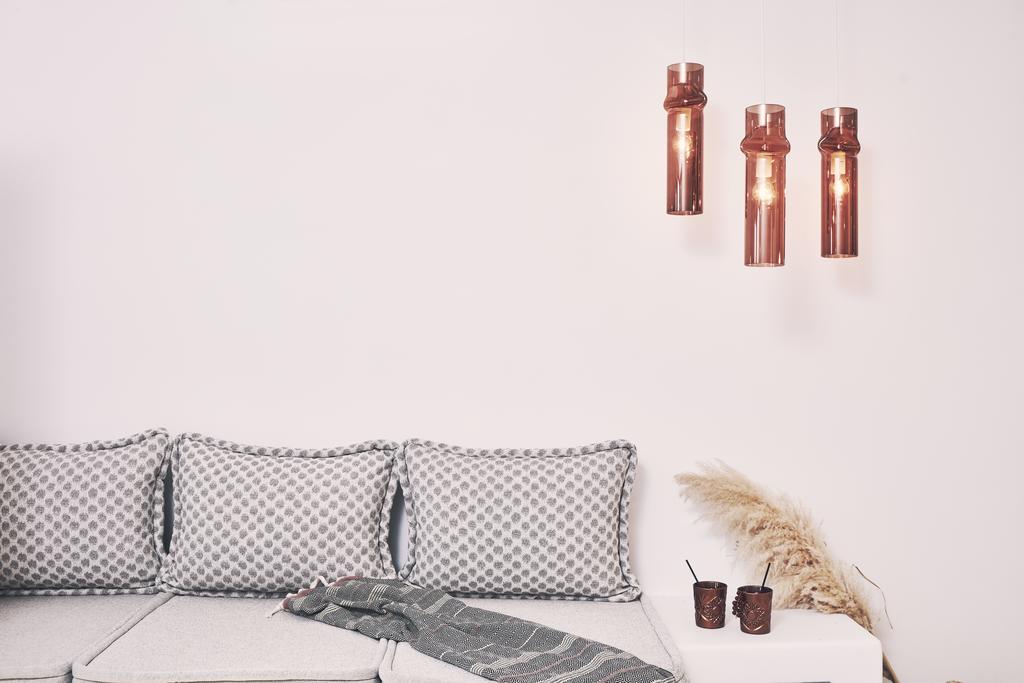A relaxed seating area is featured with a light gray sofa adorned with patterned cushions. Three pendant lights hang above, illuminating the space with a warm glow. A small table holds two dark-colored cups and a decorative plant arrangement, alongside a cozy blanket draped over the sofa.