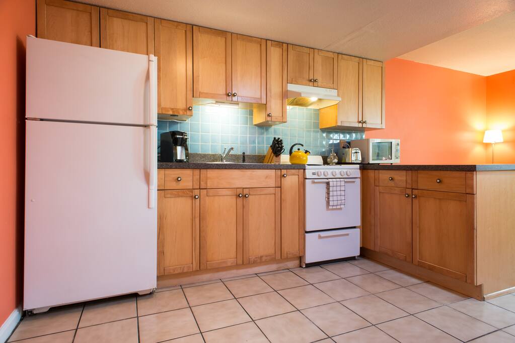 Full kitchen with refrigerator, coffee maker, stove, and pots and pans.