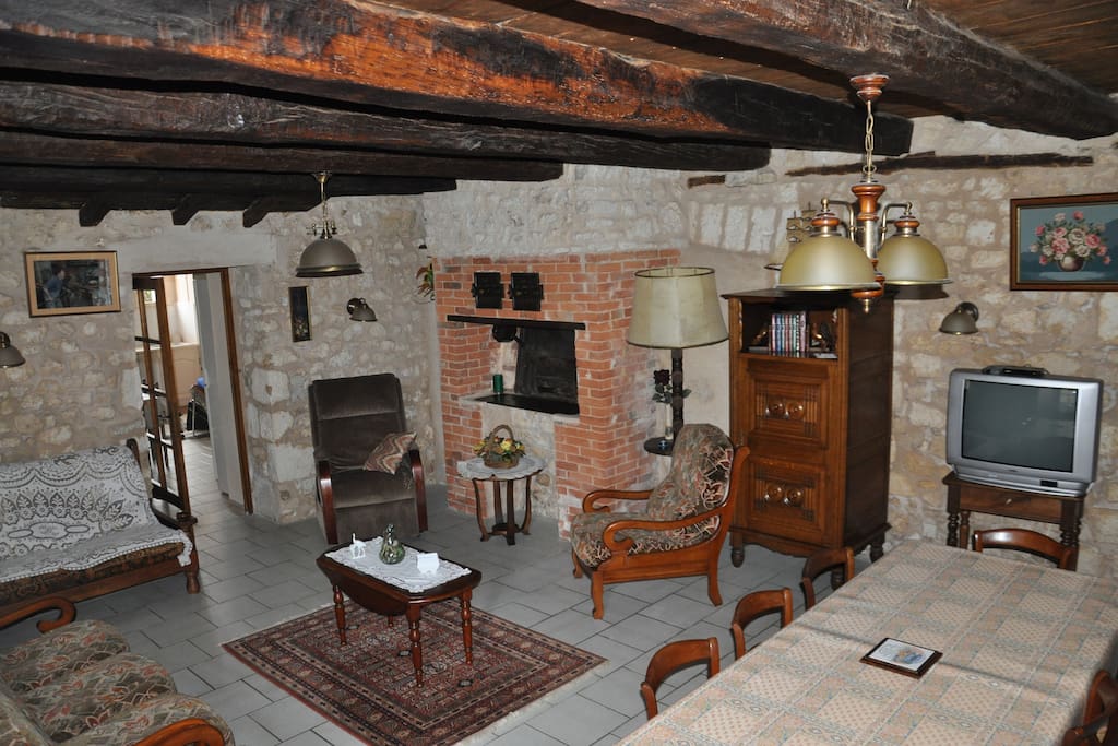 Espace convivial de 35 m2, pièce rustique, atypique devant ancien four à pain, murs en pierres apparentes et vieilles poutres au plafond, avec 2 banquettes et 3fauteuils + télé + grande table