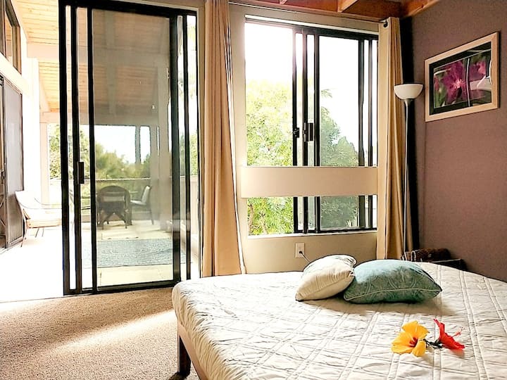 Queen size bed connected to terrace and a view of tropical green trees.