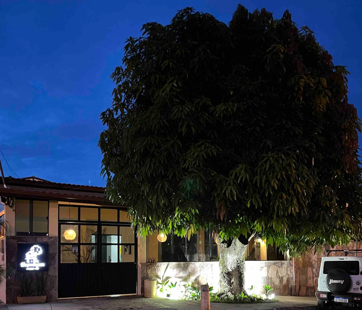 The exterior of the property is highlighted by a large, mature tree, providing a natural focal point. The building features large glass windows, with soft lighting illuminating the surroundings. The entrance is welcoming, contributing to the overall charm of the location.