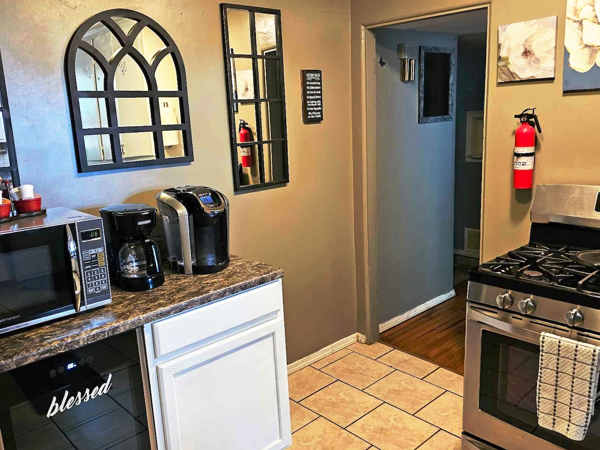 The kitchen features a mix of modern appliances, including a coffee maker, microwave, and a metal oven. A tiled backsplash complements the dark countertops. A decorative mirror and wall art add visual interest to the space. A fire extinguisher is mounted for safety.
