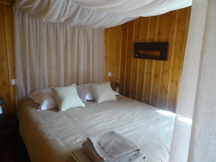 เตียงหลักเตียงขนาดควีนไซส์ตั้งอยู่ในซุ้มที่แยกออกจากพื้นที่นั่งเล่นโดยมีผ้าคลุมเตียงบางๆ