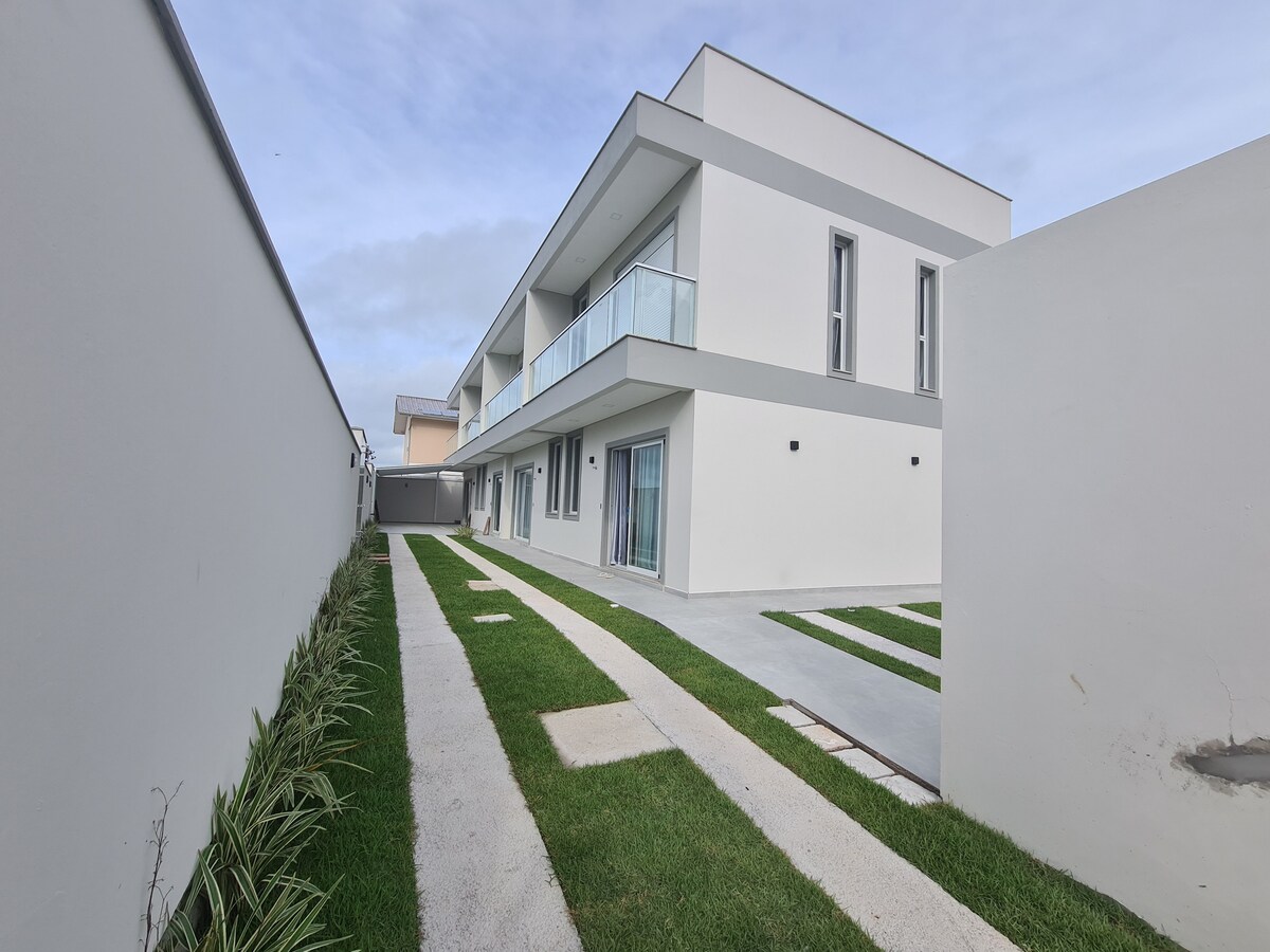 A modern two-story building features a sleek exterior with large glass doors and windows. A well-maintained pathway is bordered by neatly trimmed grass on both sides, leading to the entrance. Gray and white tones dominate the facade, contributing to a contemporary design.