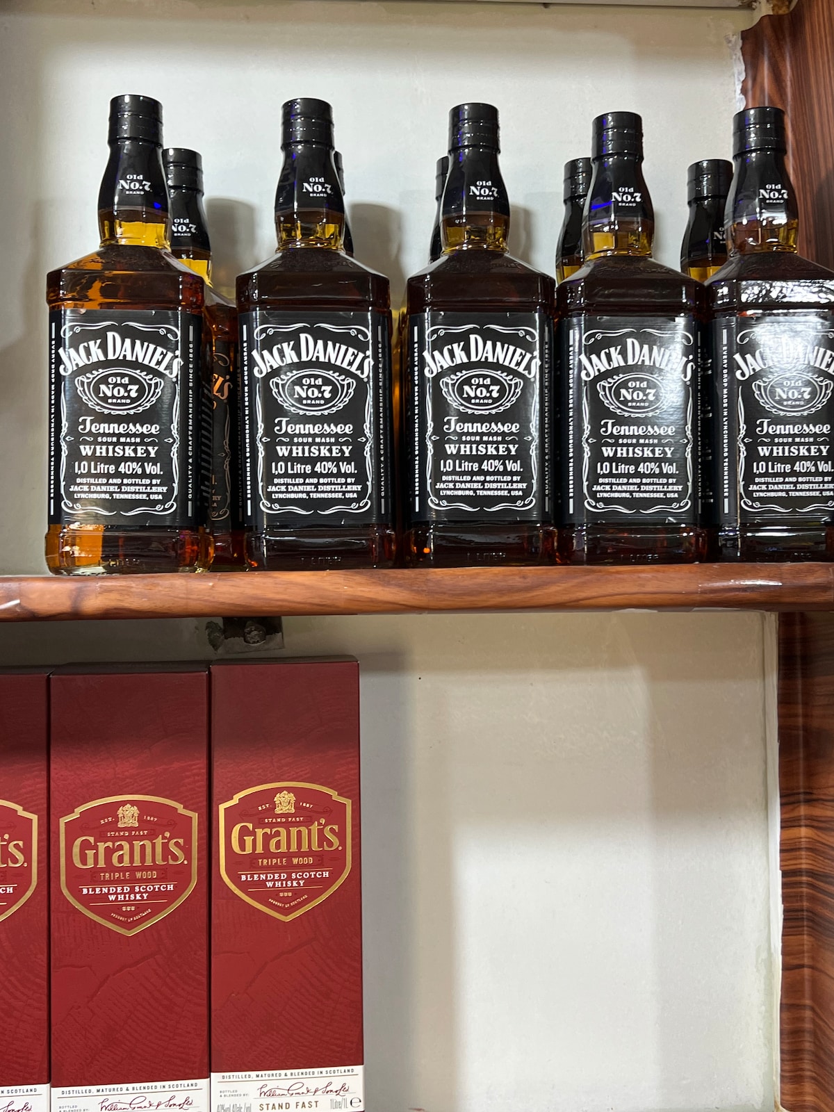 A wooden shelf displays several bottles of Jack Daniel's Tennessee Whiskey in a neat arrangement. The labels provide clear information, including brand and alcohol content. Below, boxes of Grant's whiskey are stacked, showcasing their distinctive red packaging.