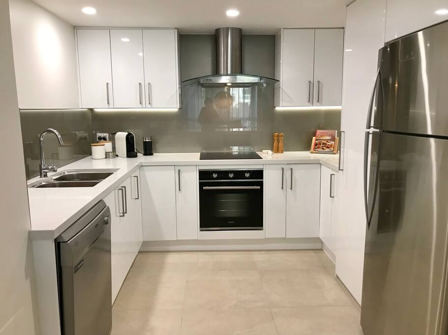 A large kitchen including a coffee pod machine, induction cooktop, dishwasher, stone bench tops, a family size fridge and much more - everything you need in a kitchen to make your stay comfortable.
