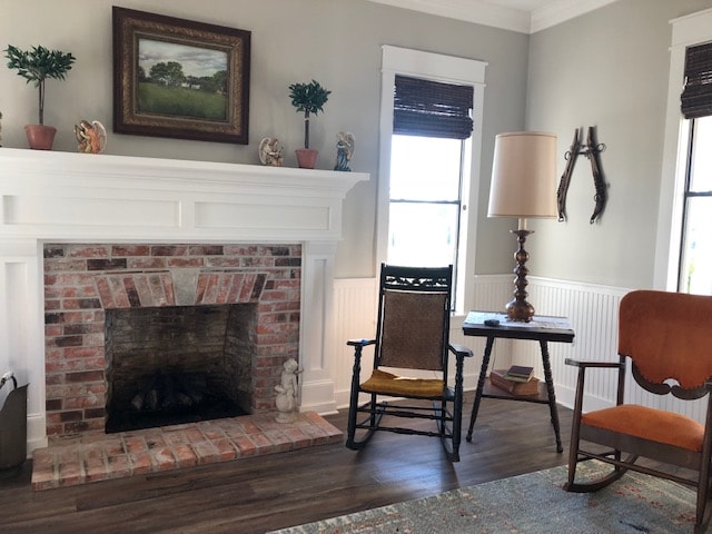 A comfortable living space features a rustic brick fireplace and a variety of seating options, including a rocking chair and an orange accent chair. Natural light enters through two windows adorned with wooden shades, enhancing the calm atmosphere.