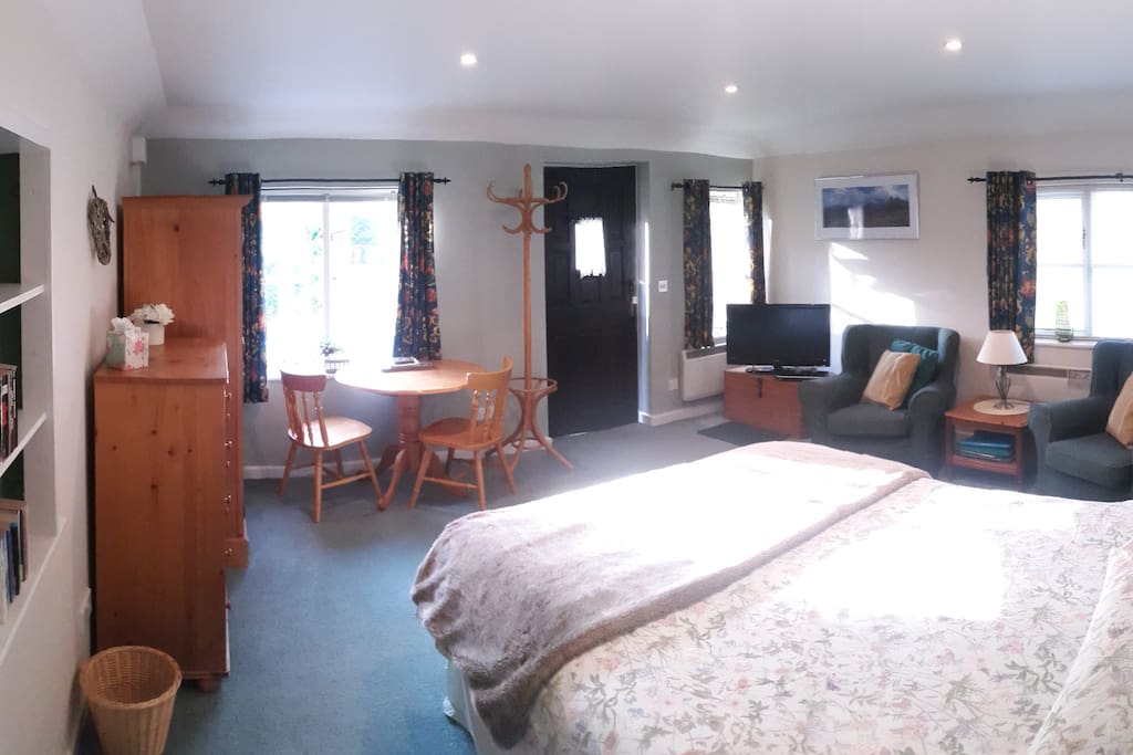 Panoramic view of main room with bed, armchairs and small dining table