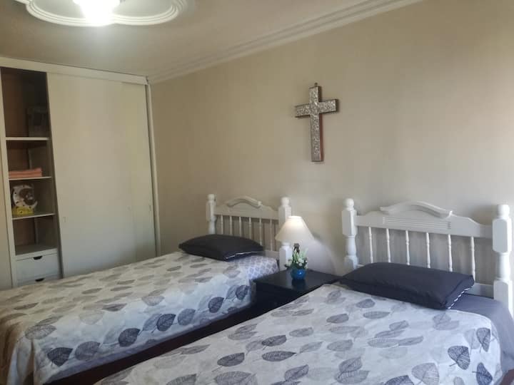 Um quarto com cama de solteiro, smartv, ventilador, armário e aquecedor. Janela com iluminação natural e ventilação.
