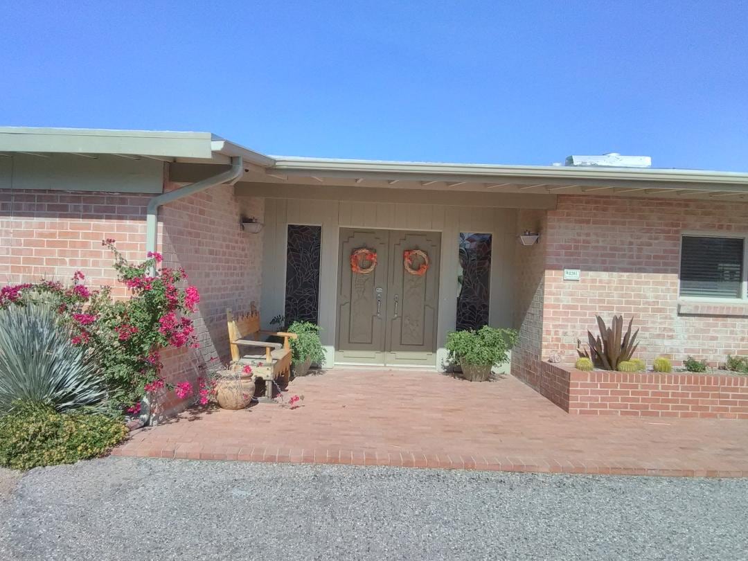 The exterior features a welcoming entrance with double doors adorned with floral details. Surrounding landscaping includes potted plants and cacti, contributing to the natural desert charm. A brick pathway leads to the front door, offering a sense of accessibility and warmth.
