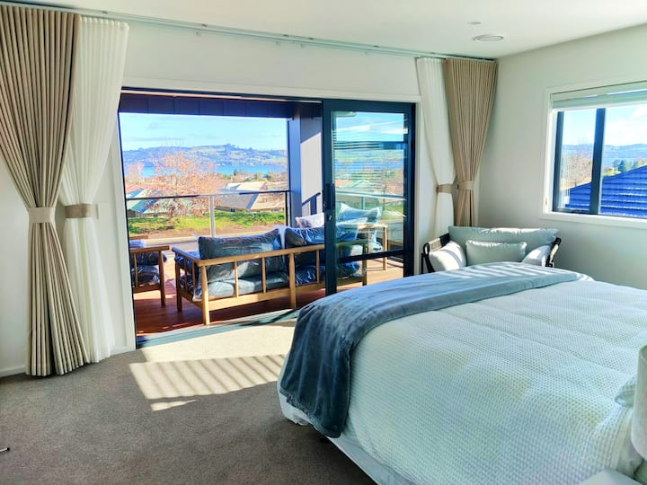 تحتوي غرفة النوم الرئيسية على باب زجاجي كبير يفتح على الشرفة في الخارج، والستائر مفتوحة للاستمتاع بالمنظر.