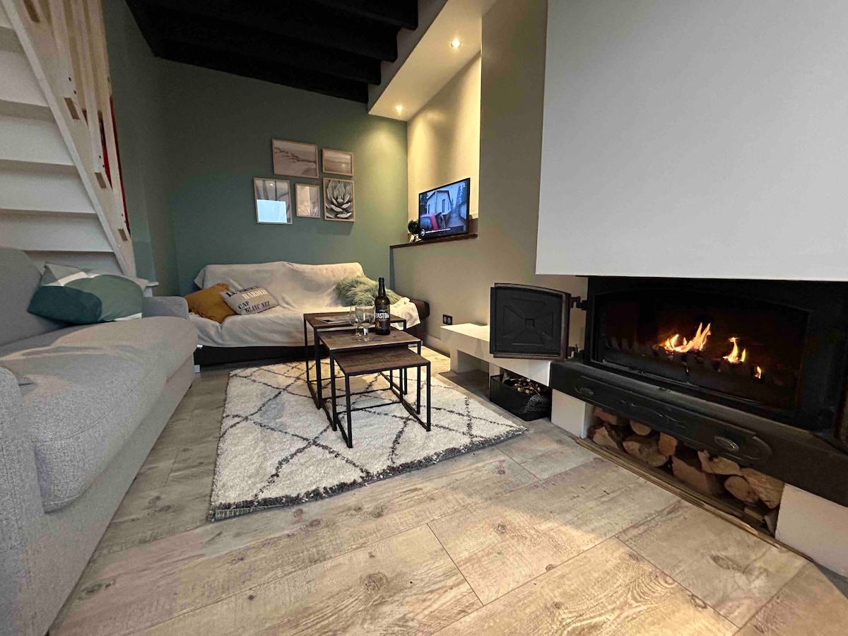 A comfortable living area features a soft gray sectional sofa and a light-colored couch, complemented by a modern coffee table. A fireplace is situated beneath a large, minimalistic white wall, while warm lighting and decorative art pieces create a welcoming ambiance.