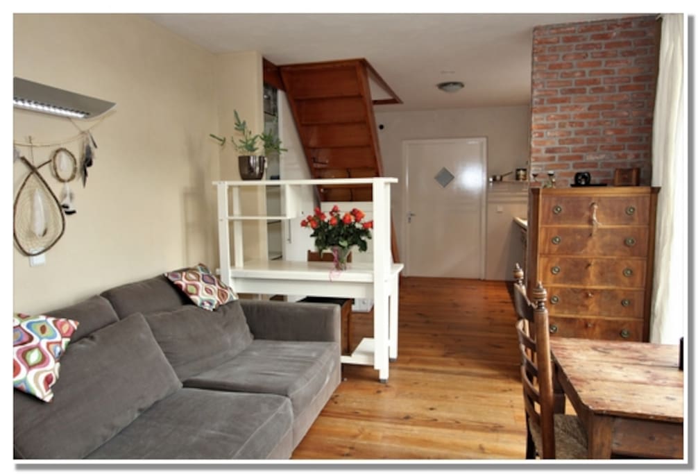 Woonkamer, rechtsvoor openslaande deuren naar buiten. Achteraan rechts de keuken. Linksachter trap naar boven (slaapkamers). Helemaal achteraan eigen entree
