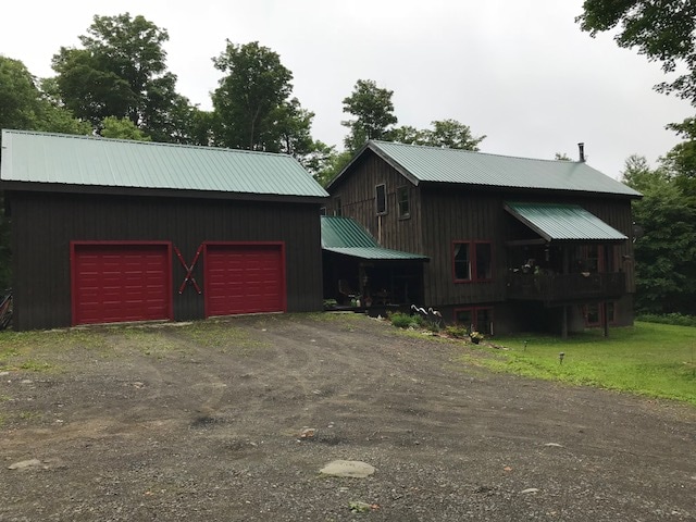 A rustic chalet is nestled among greenery, featuring a dual-garage structure on the left with red doors and a distinct green metal roof. The main building, showcasing multiple levels, is adorned with a dark wooden facade and red accents, welcoming guests into a tranquil woodland setting.