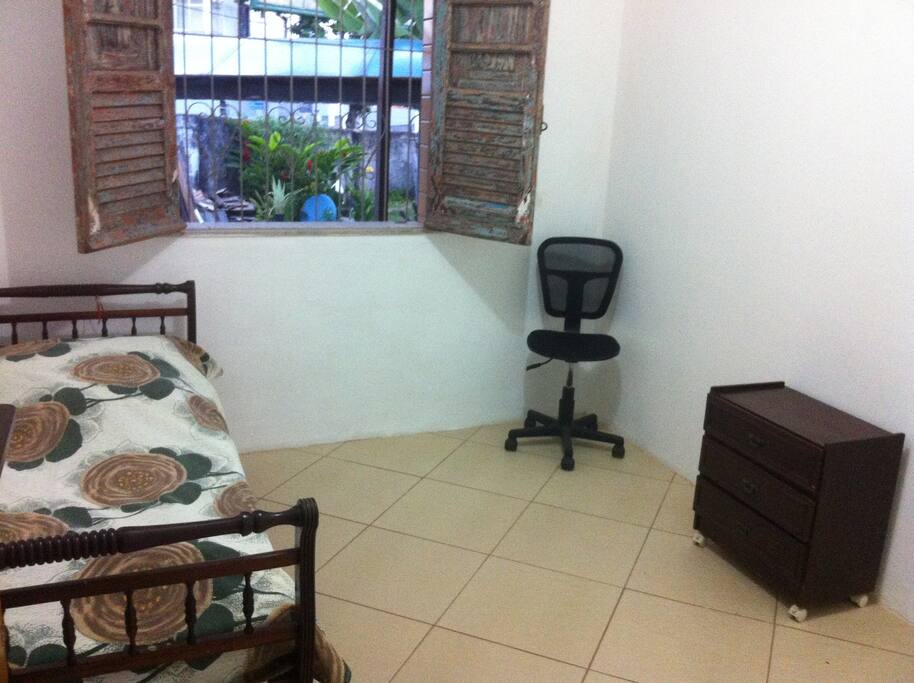 Quarto com uma cama de solteiro, ventilado com um criado mudo e uma arara para roupas