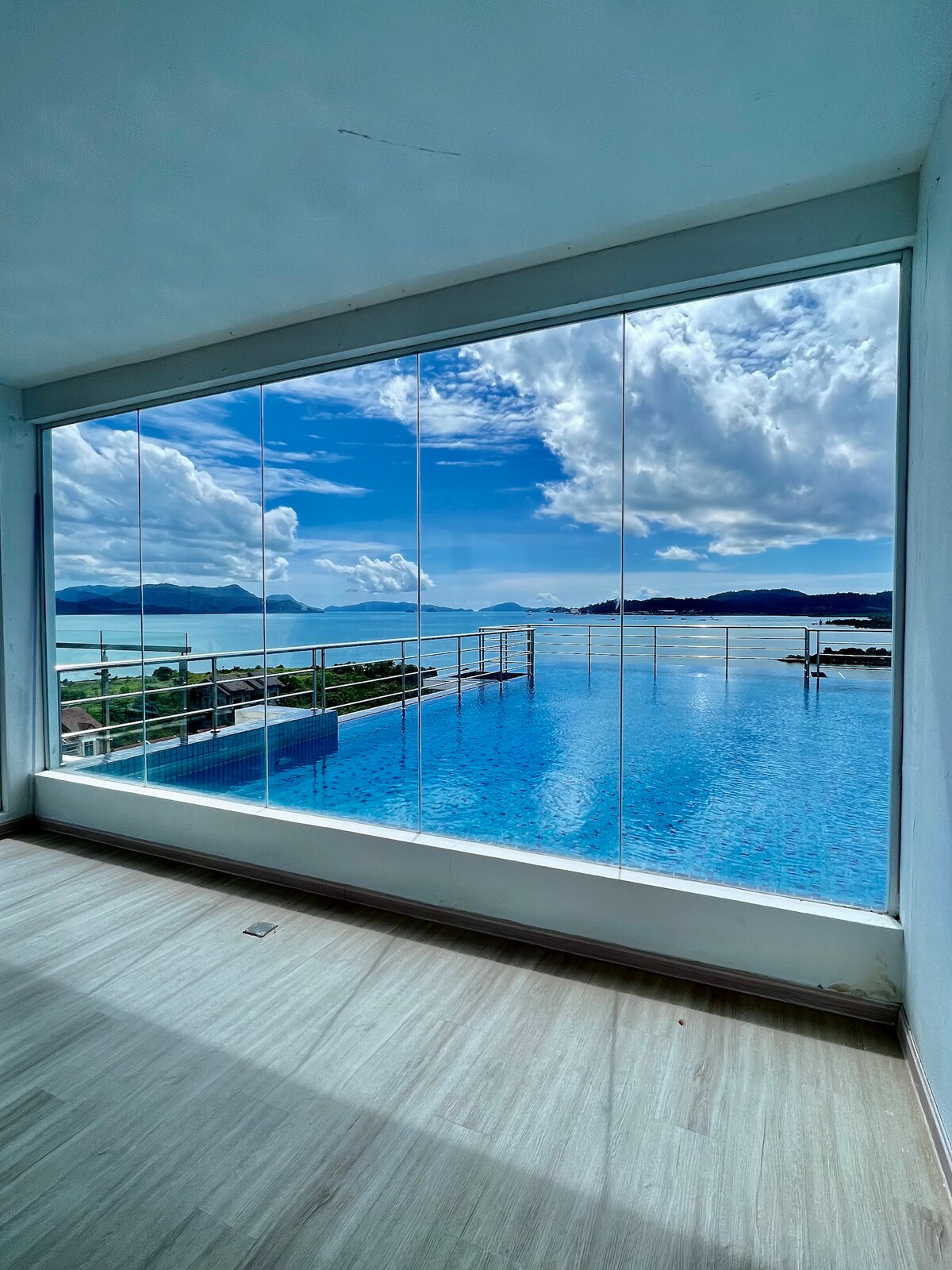 A spacious window captures expansive views of the sea and sky with clouds reflecting over the water. The rooftop infinity pool is visible, blending seamlessly into the horizon, creating a serene atmosphere.