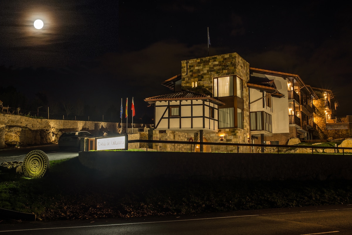 The exterior of a well-designed building is illuminated under a full moon, showcasing a mix of stone and wooden elements. Soft lighting highlights the entrance and surrounding details, while a tranquil atmosphere is enhanced by the night sky.