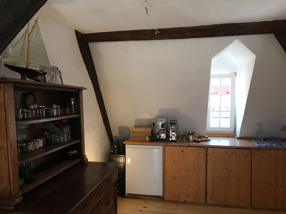 Blick aus Wohnraum in die Küche. Links eine große Auswahl an Gewürzen, leiser Kühlschrank, Toaster, Arbeitsplatte zum Kochen.
(English: View in the kitchen area. Quiet fridge, spices, toaster and worktop for food preparing)