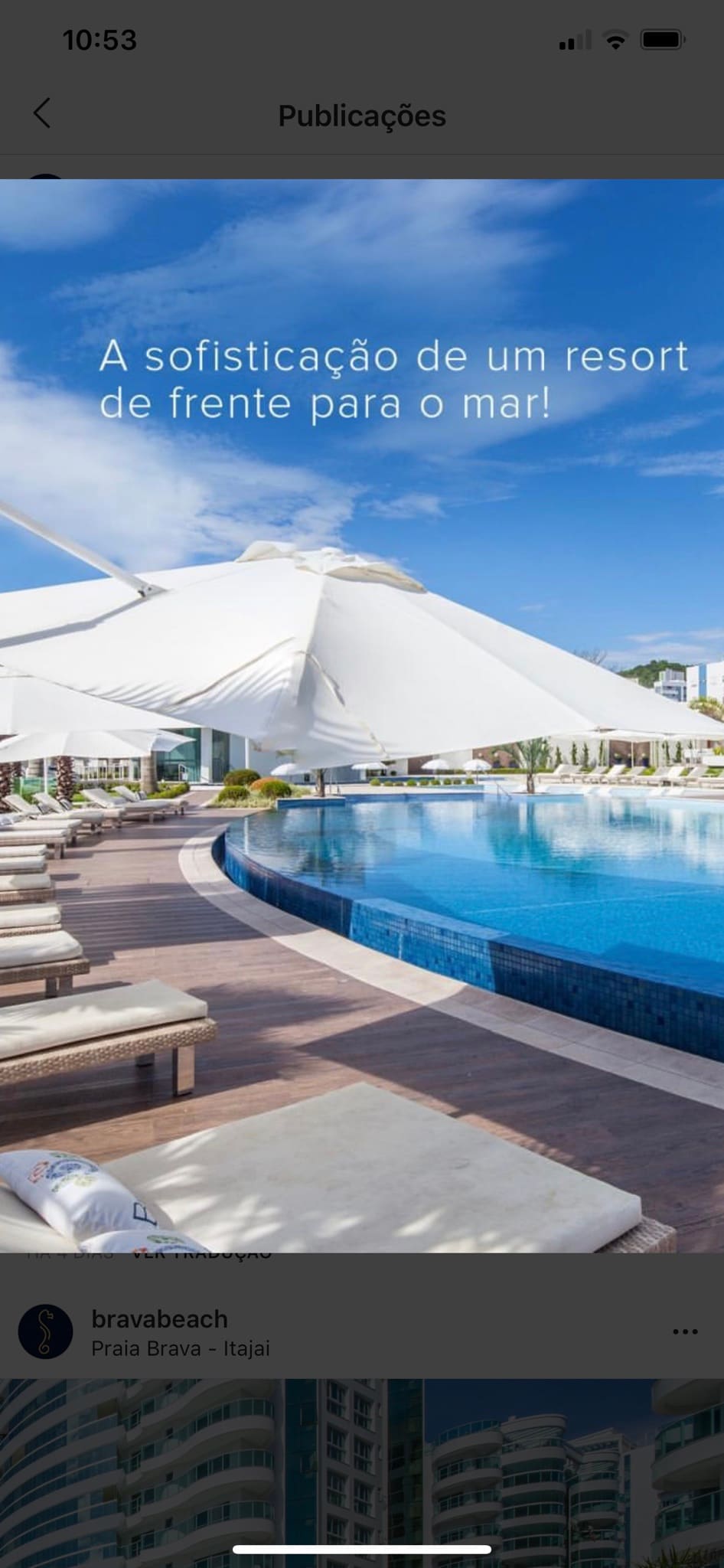 An outdoor pool area features lounge chairs arranged around a spacious swimming pool, under a large white canopy. The ocean is visible in the background, and the setting reflects a resort-like atmosphere with well-maintained landscaping.