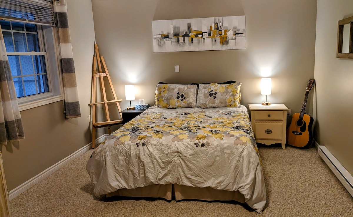 Comfortable queen bed, an easel for doodling and an old twelve-string for noodling. The window looks out into the screened porch. 