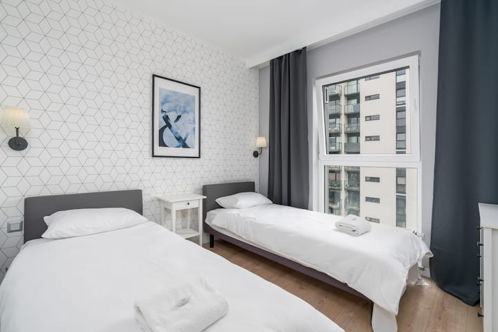 Spavaća soba s dva kreveta za jednu osobu, neutralnim tonovima i zidnim umjetničkim djelima iznad kreveta.