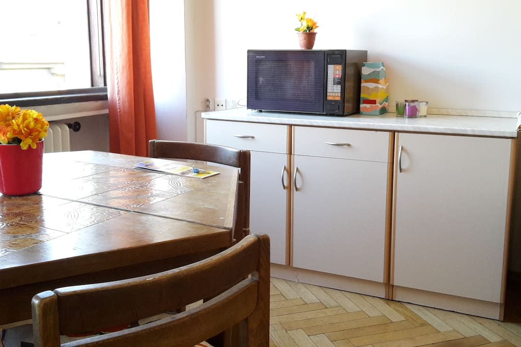 On this wall there is a kitchen counter with a microwave and cooking equipment and kitchenware. Large table in the middle of the room.
