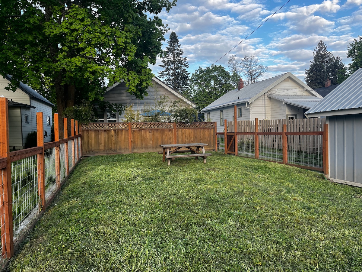 A fenced outdoor space features a grassy area with a picnic table in the center. Surrounding fences create a sense of privacy, while trees and neighboring houses provide a natural backdrop. The space is open and ideal for leisure and pet-friendly activities.