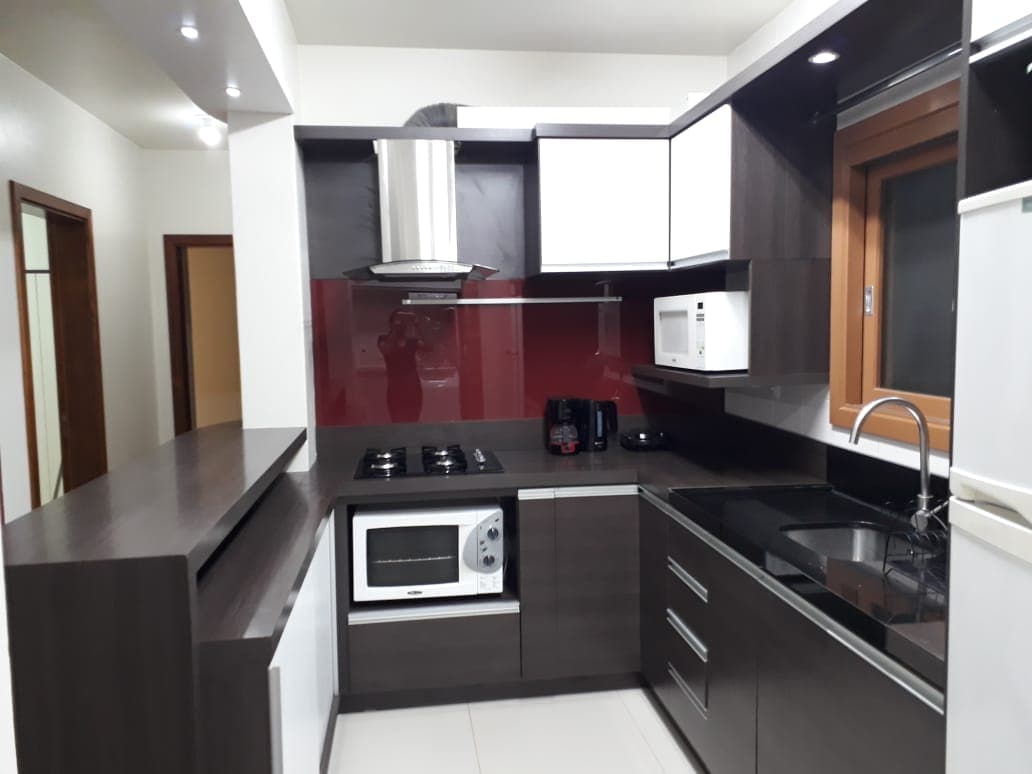 The kitchen is designed with modern cabinetry in dark tones, complemented by a contrasting red backsplash. A gas cooktop, microwave, and a sleek kitchen sink are visible. Adequate counter space is available, along with essential appliances such as a coffee maker and a toaster.