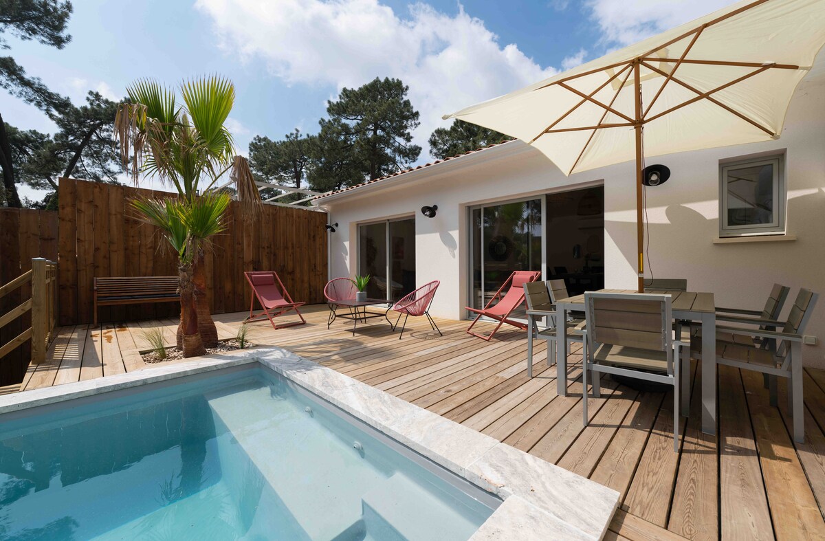The outdoor terrace features a private pool surrounded by wooden decking. Comfortable chairs are arranged under a large umbrella, while a small palm tree adds a touch of greenery. Large sliding glass doors provide access to the interior space.