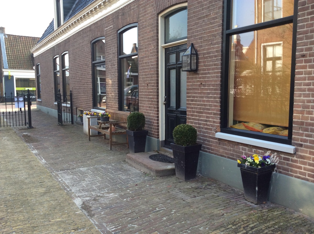 An inviting exterior is presented with a brick facade, featuring large windows that allow natural light to enhance the space. Two flower pots with colorful blooms flank the entrance, accompanied by a wooden bench, creating a welcoming atmosphere.