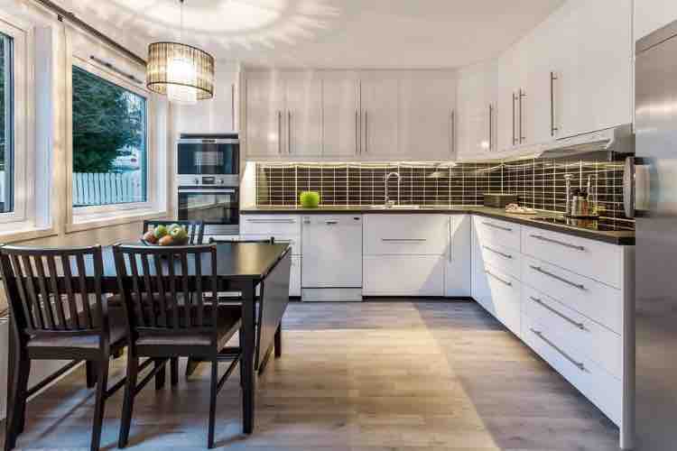 The kitchen features a modern design with white cabinetry and black countertops. A dining table with four chairs is positioned near large windows, allowing natural light to brighten the space. Stainless steel appliances are integrated seamlessly into the cabinetry, enhancing the contemporary look.