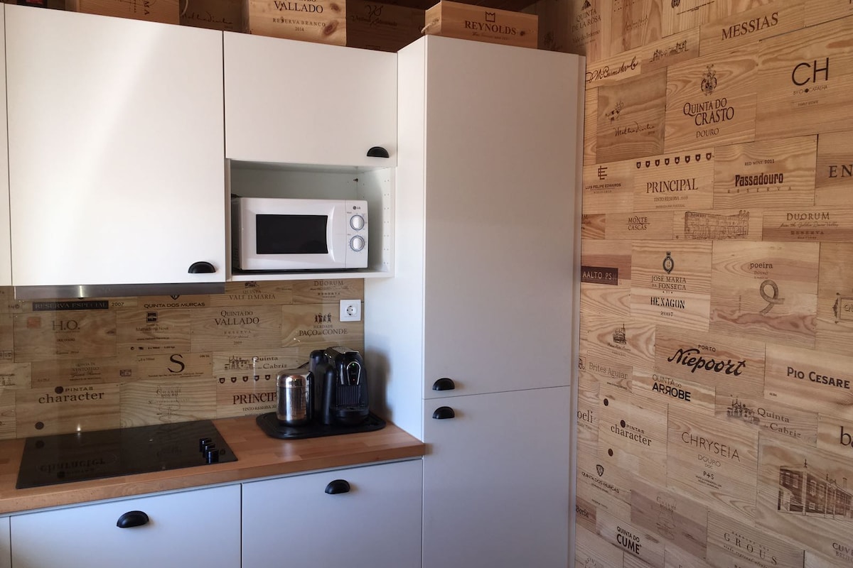 A compact kitchen features modern cabinetry with a wood-patterned accent wall. Essential appliances include a microwave and coffee machine positioned on a wooden countertop. The space is efficiently designed for convenience while maintaining a stylish and functional atmosphere.