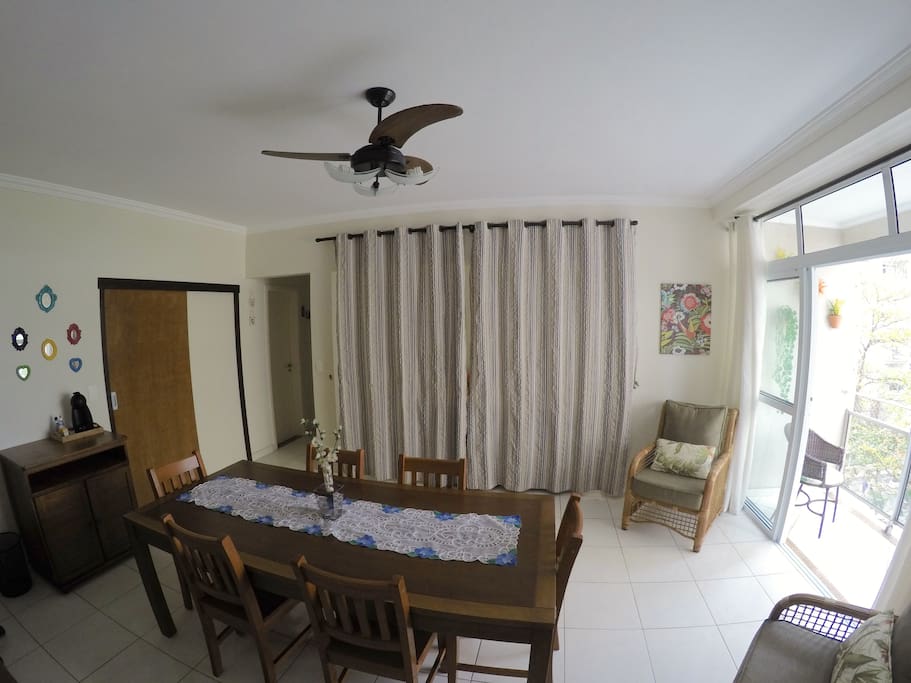 Sala de jantar: acesso à cozinha (esquerda), acesso à sala de TV/quarto reversível (atrás das cortinas no centro), sacada (direita)
