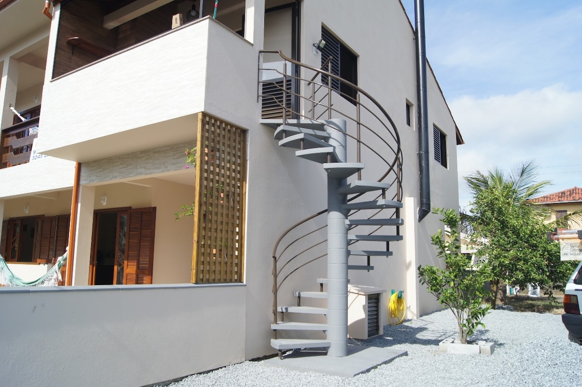 A spiral staircase is prominently featured at the exterior of the building, connecting multiple levels. The staircase's sleek gray design contrasts with the lighter wall, bordered by a pebbled area and small greenery, providing a functional and aesthetic element to the property.