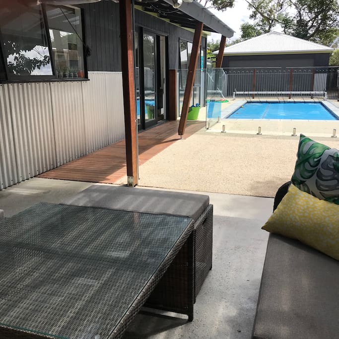 Outdoor covered BBQ area with sofa style seating, small bar fridge, and Weber overlooking the pool