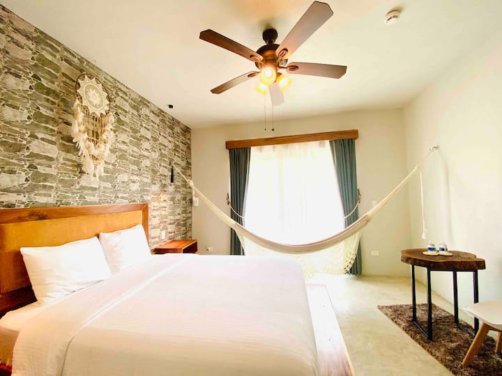 Ბამბის კოტეჯი ხელნაკეთი ჰამაკით, რომელიც ბაღს გადაჰყურებს.