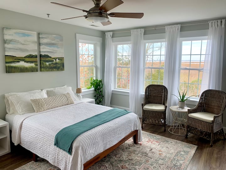 Bedroom area with nightstands, small siting area, ceiling fan, and windows overlooking the sound