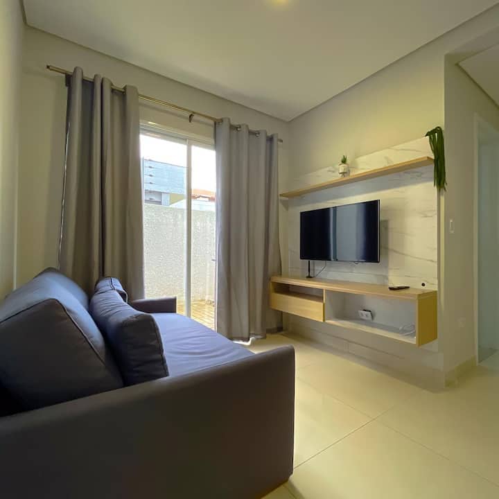 Sofá cama doble, sala de estar con salida para el área de jardín y estante con TV.